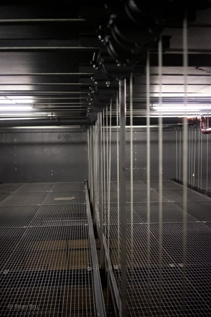Et bilde fra et teknisk område over en scene (snoreloft). Gulvet består av metallrister, og en lang rekke med stålwirer strekker seg vertikalt fra trinser i taket og ned gjennom åpninger i gulvet.